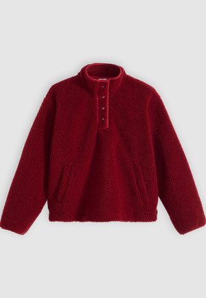 Roter Fleecepullover mit hohem Kragen und Vier-Knopf-Leiste, ausgestattet mit zwei Seitentaschen und einer weichen, strukturierten Oberfläche.