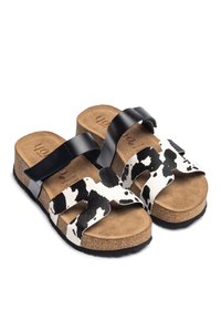 Black and white cow print sandals with a cork sole, featuring dual straps made of smooth leather and a soft suede insole.