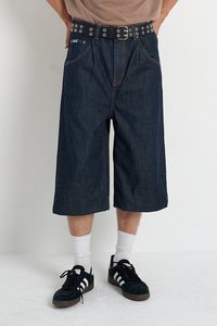 Traperice kratke hlače s slobodnim krojem, tamnim pranje i širokim nogavicama. Imaju crni remen s metalnim rupama. Nosive s bijelim čarapama i crnim tenisicama.