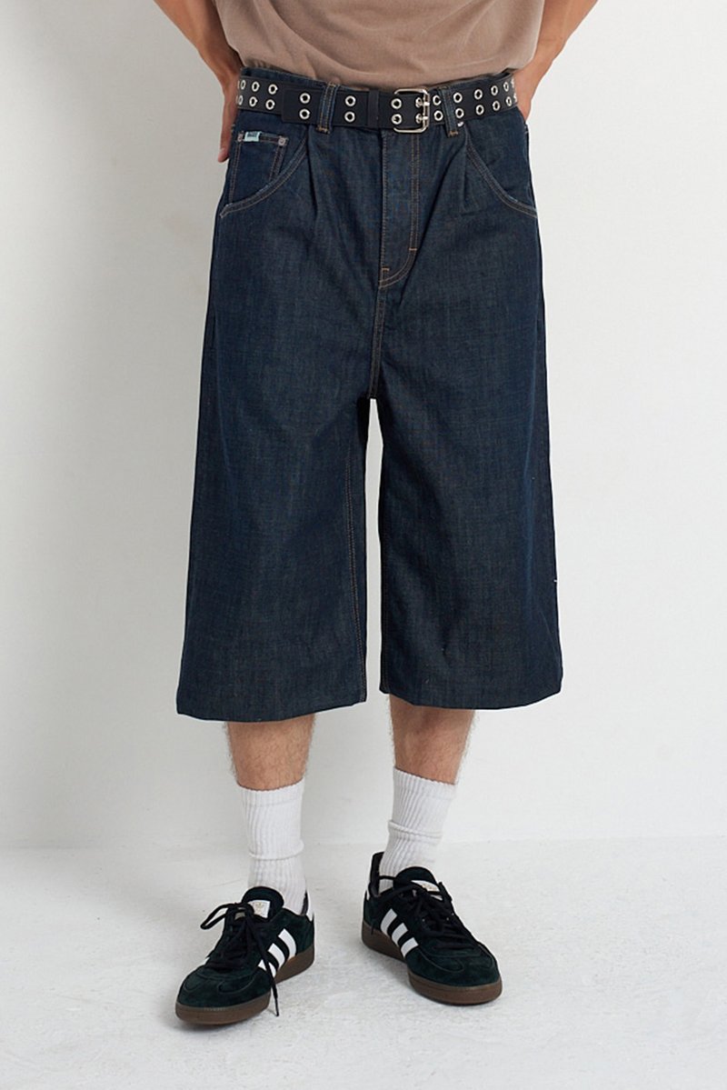 Traperice kratke hlače s slobodnim krojem, tamnim pranje i širokim nogavicama. Imaju crni remen s metalnim rupama. Nosive s bijelim čarapama i crnim tenisicama.