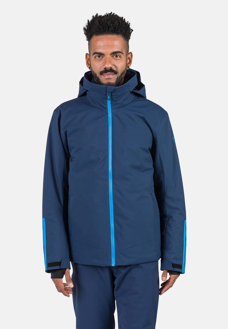 Marineblauer wasserdichter Jacke mit blauem Reißverschluss und Akzenten. Verfügt über eine Kapuze, elastische Bündchen und eine seitliche Reißverschlusstasche. Glatte Textur, modernes Design.