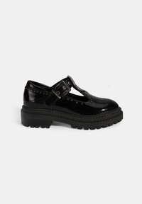 Zwarte gepatineerde leren T-strap schoen met metalen studs, chunky zwarte zool en verstelbare gesp met een gestructureerde band.