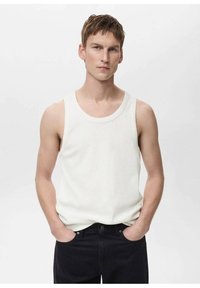 Witte mouwloze tanktop van ribbelstof, ronde halslijn, aansluitend ontwerp. Gecombineerd met donkerdenim jeans, staand tegen een simpele achtergrond.