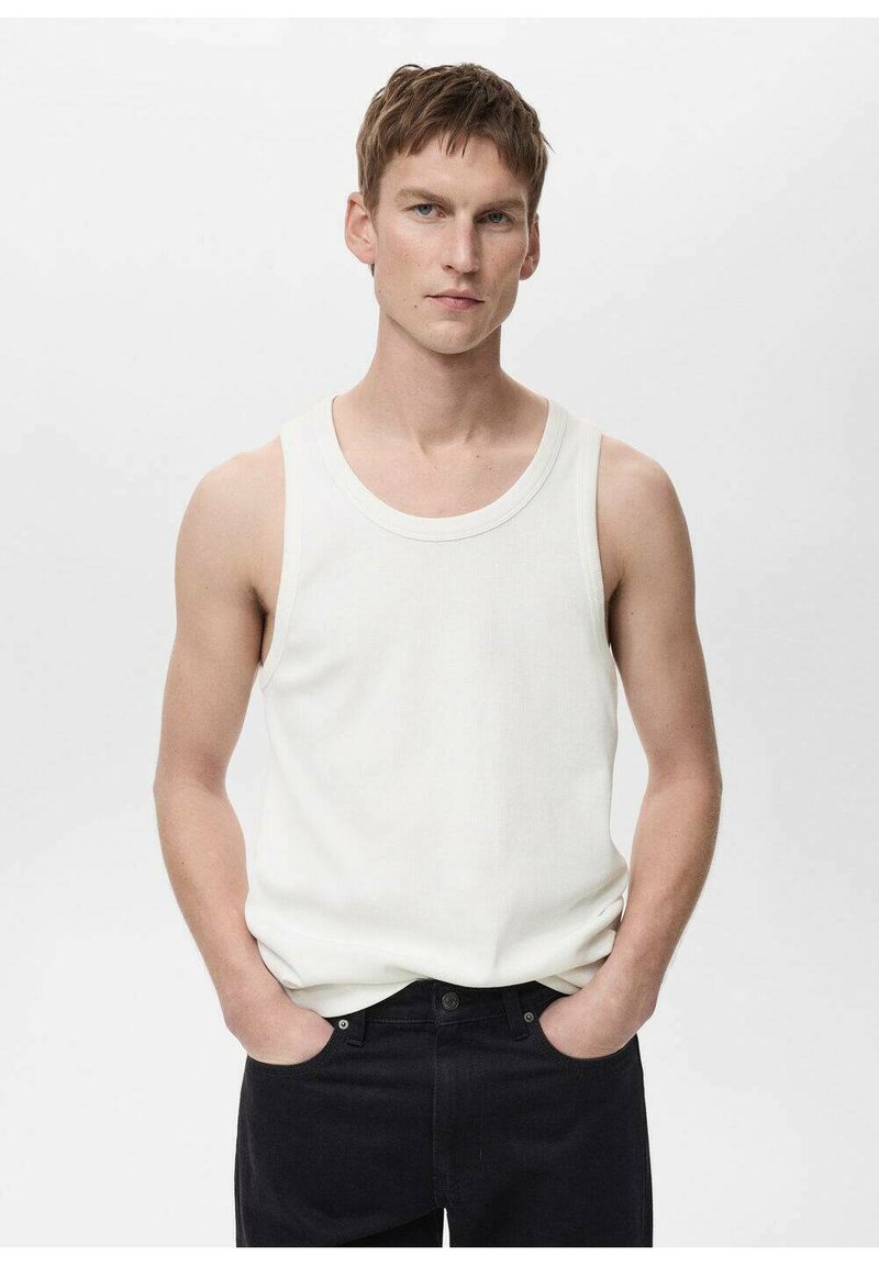 Witte mouwloze tanktop van ribbelstof, ronde halslijn, aansluitend ontwerp. Gecombineerd met donkerdenim jeans, staand tegen een simpele achtergrond.