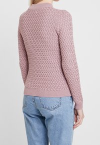 Pink knitted sweater with a textured diamond pattern, ribbed neckline, cuffs, and hem. Paired with light blue denim jeans.