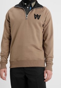 Brązowa bluza na zamek z czarnym kołnierzem, z wyszywanym logo "AA" na piersi. Materiał o fakturze z prążkowanymi mankietami i dołem.