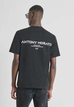 Zwarte katoenen T-shirt met korte mouwen, voorzien van witte bedrukte tekst op de achterkant: "ANTONY MORATO OPGERICHT TWEEDUIZEND ZEVEN AM."
