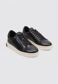 Zapatillas de cuero negro con acabado suave, punta redonda, cordones negros y suela de goma crema. Presentan un diseño aerodinámico y perfil bajo.