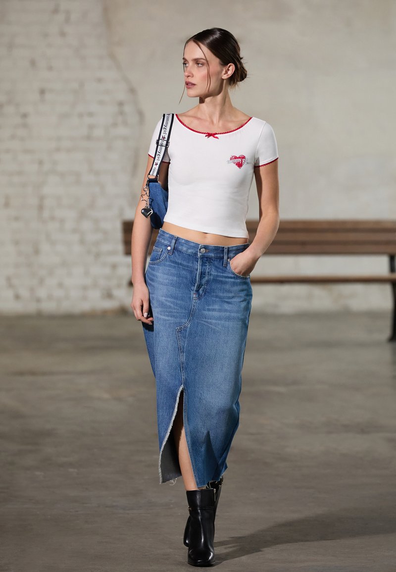 Hvit cropped topp med rød kant, med et hjerte grafikk. Lys blå denim skjørt med slisse foran og frynset kant. Svarte ankel støvler.