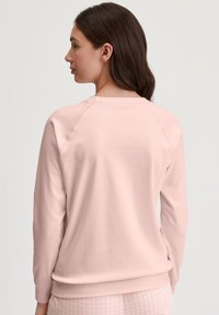 Lichtroze sweatshirt met een ronde hals, raglanmouwen en een zachte textuur. Heeft een casual pasvorm en ribgebreide boorden en onderkant.
