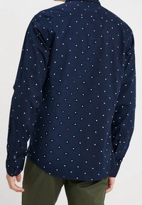 Mørkeblå skjorte med knapper og tekstureret stof, prydet med farverige polkaprikker i rød, hvid og blå. Slank pasform med knappede manchetter og krave.