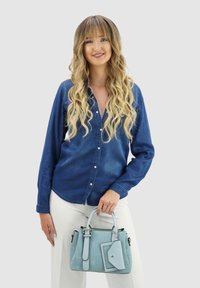 Denim shirt met knopen aan de voorkant, lange mouwen en een relaxte pasvorm; houdt een lichtblauwe handtas vast met een afneembare zak en zilveren hardware.
