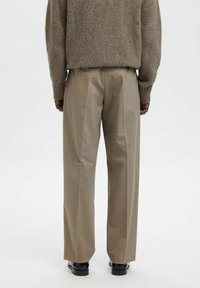 Beige ullgenser med ribbestrikkede mansjetter, over lysegrå vid bukser med myk tekstur og et subtilt rutemønster.