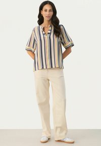 Stribet skjorte i nuancer af navy, pink og gul med en notch krave. Parret med lyse beige bredde ben bukser og hvide sneakers.