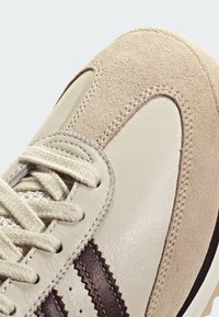 Teniska z béžové semiše a kůže s hnědým cikcak pruhem, texturovanými šňůrkami a hladkou gumovou podrážkou.