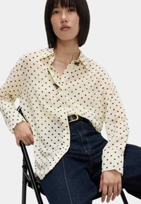 Blusa crema a pois con colletto, chiusura a bottoni e maniche lunghe, abbinata a jeans in denim scuro a vita alta.