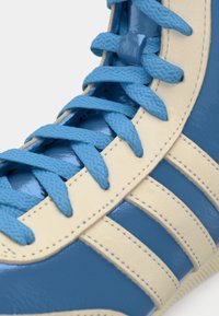 Blue patent leather sneaker with light beige accents, featuring laces in matching blue and three horizontal stripes in beige.