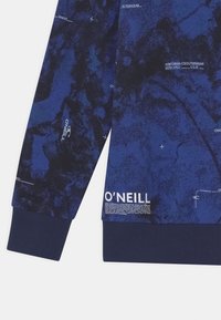 Felpa blu navy con un motivo testurizzato, polsini a coste e dettagli di branding stampati. Il materiale sembra morbido e tessuto.