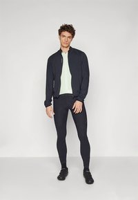 Sportjacka i marinblått, figurnära mintgrön topp och svarta leggings, med cykelskor. Har dragkedjeförslutning och en slank design.