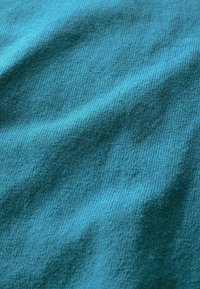 Törökzöld textil sima textúrával, amelyen finom, egységes bordázási mintázat fut végig, így diszkrét mélységet és dimenziót teremt.
