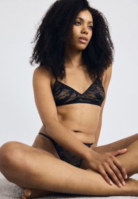 Zwart kanten lingerie set met een triangle bralette met dunne bandjes en een bijpassende tangaslip, beide met een bloemenpatroon.