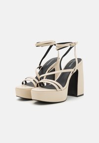 Μπεζ πλατφόρμες με φαρδιές λωρίδες, κούμπωμα στον αστράγαλο και παχύ τετράγωνο τακούνι. Λείος υφασμάτινος σχεδιασμός με μαύρο εσωτερικό και μινιμαλιστική αισθητική.