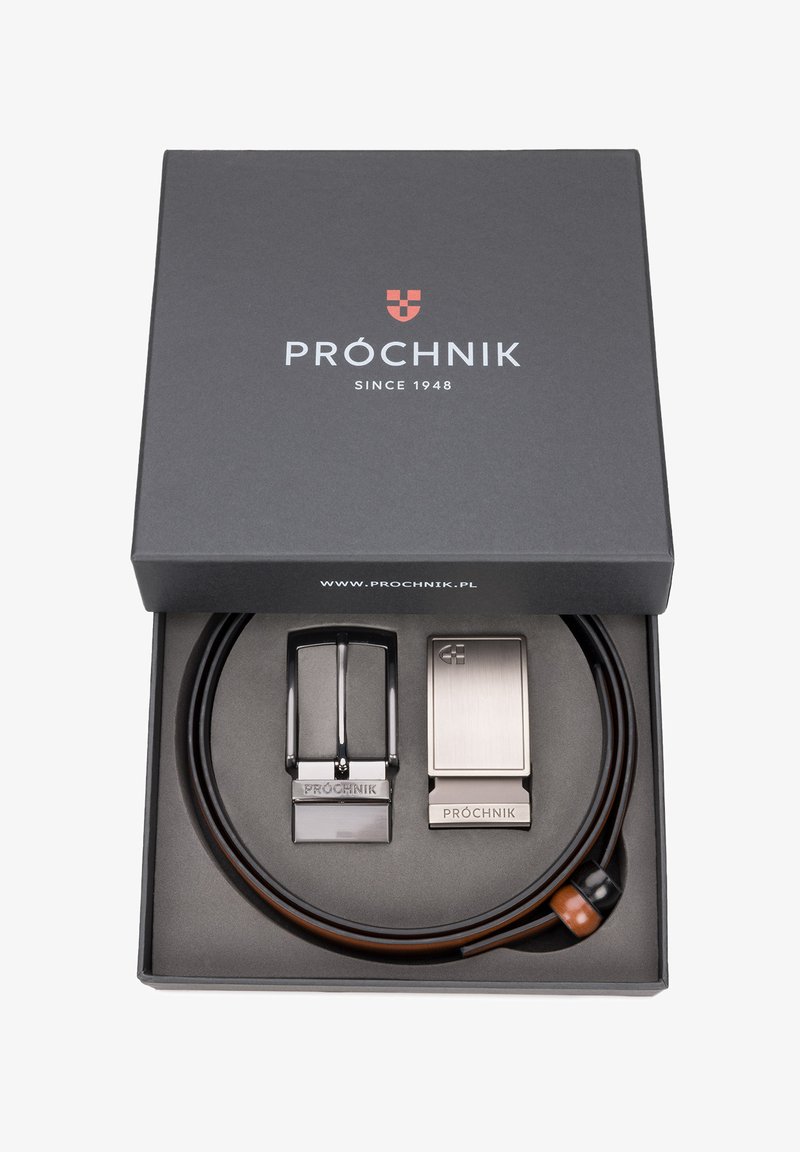 Czarny skórzany pasek z dwiema metalowymi klamrami w czarnym pudełku. Jedna klamra jest błyszcząca srebrna, a druga ma matowe wykończenie, obie są grawerowane.