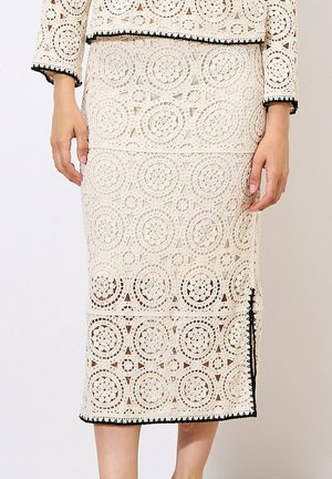 Gonna midi in pizzo color crema con motivi circolari, rifinita con dettagli neri. Presenta una silhouette aderente e uno spacco laterale.