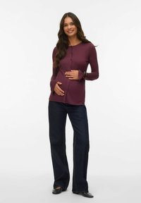 Graviditet långärmad topp i djup burgundy med knappar och utsvängda ärmar, matchad med mörka denim vidbyxor. Slät, elastisk tyg.