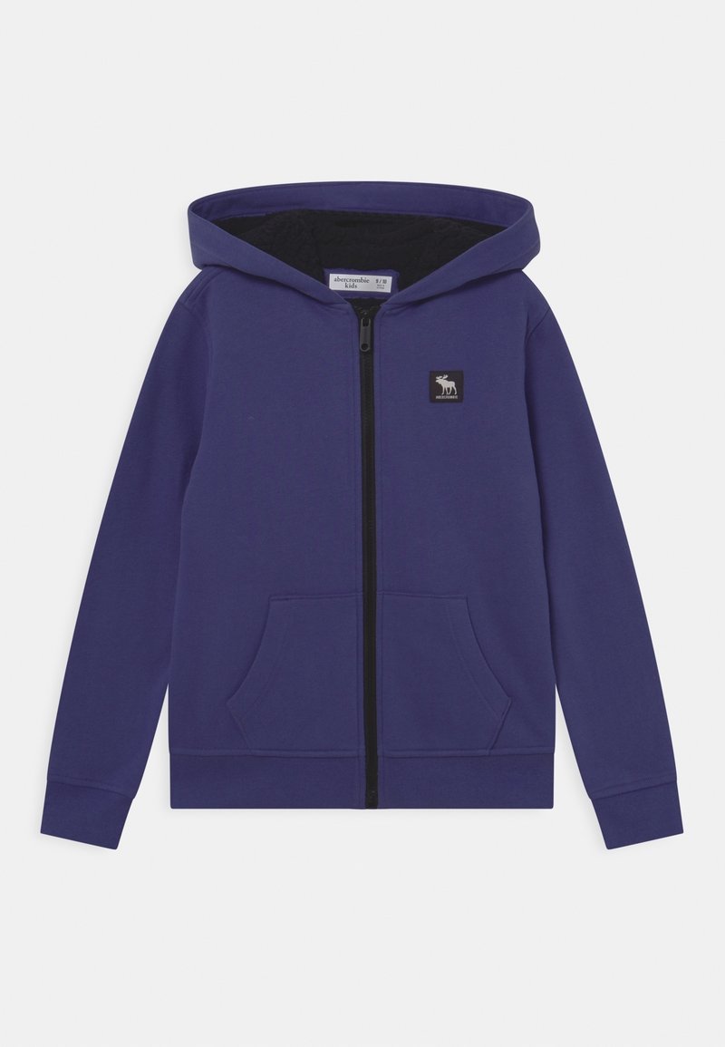 Sudadera morada con cremallera, forro negro, dos bolsillos frontales y un pequeño parche con logo. Material de algodón, corte estándar, capucha ajustable.