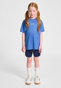 Niebieska, paskowana koszulka sportowa o luźnym kroju, w połączeniu z granatowymi szortami. Białe skarpetki do kostki i jasne sneakersy z czarnymi akcentami dopełniają całość.