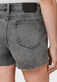 Shorts en denim noir avec un ourlet effiloché, dotés d'une poche arrière et d'une étiquette en cuir noir. La texture est lisse avec une couture classique.