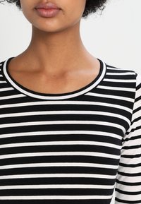 Musta-valkoinen raidallinen paita, jossa on pyöreä pääntie ja pitkät hihat, valmistettu pehme ästä ja joustavasta kankaasta.