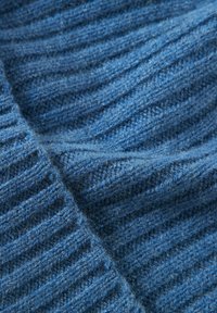 Tessuto a maglia blu con una finitura morbida e testurizzata. Il materiale mostra spessori variabili nelle coste, indicando elasticità.