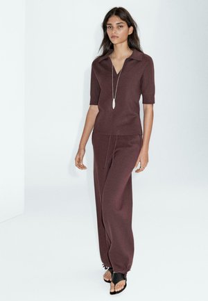 Ensemble deux pièces bordeaux comprenant un haut polo à manches courtes et un pantalon à jambes larges. Le tissu a une texture lisse, avec des cordons de serrage à la taille.