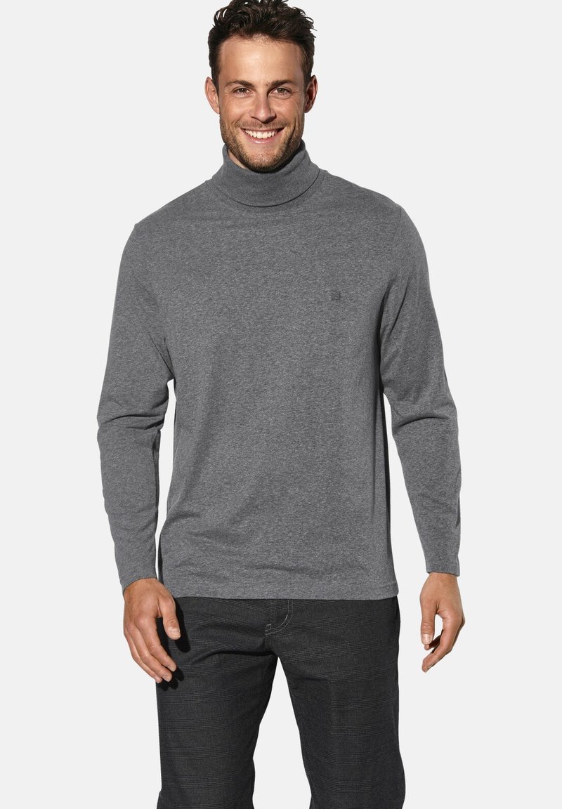 Grauer Rollkragenpullover mit langen Ärmeln, aus weichem Stoff. Mit einem dezenten Logo auf der Brust, kombiniert mit dunkler Jeans.