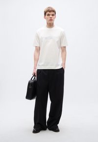 Άσπρο κοντομάνικο μπλουζάκι με γραφικό σχέδιο στο μπροστινό μέρος, συνδυασμένο με μαύρο παντελόνι φαρδύ και μαύρη τσάντα. Μαύρα παπούτσια.