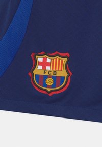 FC Barcelonan logo tummansinisen polyesterikankaan päällä. Logossa on kilven muoto, jossa on punaisia ja keltaisia raitoja, valkoinen risti ja jalkapalloikoni.