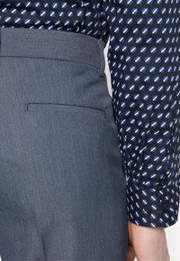 Blå mönstrad skjorta med lång ärm bredvid grå skräddarsydd byxor med en slät textur och en bakfickadetalj.