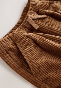 Hnedá kordová sukňa so zvislou rebrovanou textúrou, opaskom na viazanie a bočnými vreckami, ktorá pôsobí mäkko a nadýchane.