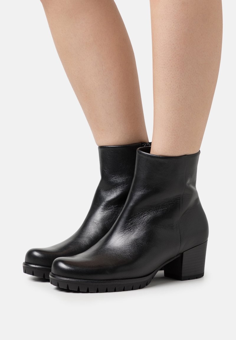 Botas de cuero negras hasta el tobillo con un acabado suave, punta redondeada y un tacón bajo y discreto. Suela de goma texturizada notable para una mejor tracción.