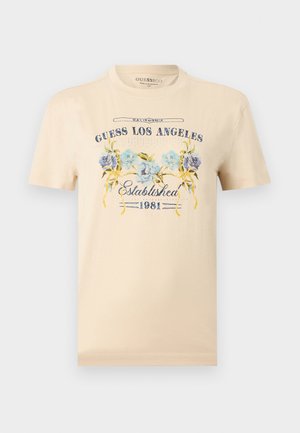 Beige T-shirt med korte ærmer og teksten "Guess Los Angeles Established 1981" samt et blåt blomsterdesign på fronten.