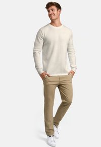 Hellbeiger Strickpullover mit strukturiertem Muster, kombiniert mit beige-farbenen Hosen und weißen Sneakers, mit lockerer Passform und Rundhalsausschnitt.