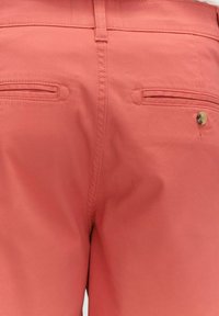 Korallfärgade shorts med ett slätt tyg, som har två bakfickor med horisontella öppningar och en liten guldknot.