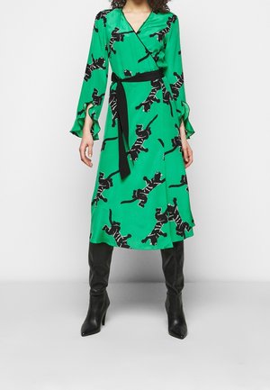 Grøn slå-om-kjole med sorte katteprint, sort taljebånd, flæser på klokkeærmerne, kombineret med sorte knæhøje støvler med hæl.