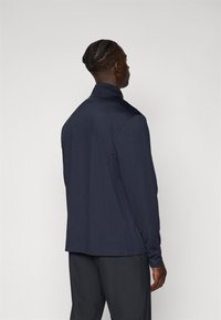 Dunkelmarineblaues Langarmshirt mit strukturiertem Kragen und glattem Stoff. Verfügt über einen lockeren Schnitt und minimale Nähdetails.