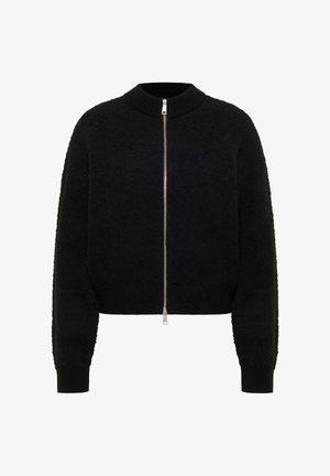 Čierna krátka bunda s chlpatou textúrou, má vysoký golier, zapínanie na zips na celú dĺžku a rebrované manžety a lem.