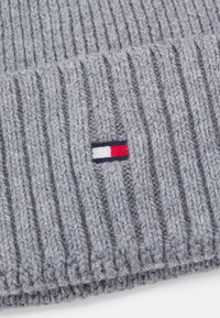 Gorro de lana gris de punto con textura acanalada. Presenta un pequeño parche de logo que consiste en franjas rojas, blancas y azules. Material de lana suave.