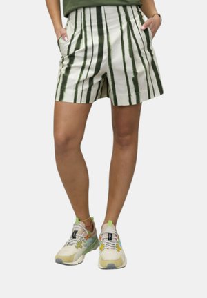 Parte inferiore del corpo con pantaloncini crema a righe verticali verde scuro e scarpe da ginnastica sportive multicolori con lacci, in piedi con le mani nelle tasche.