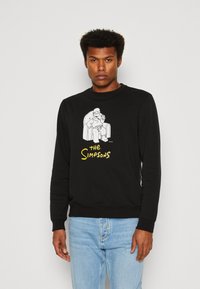 Sudadera negra con un gráfico blanco de un personaje sentado, con el texto "Los Simpson" en amarillo. Cuello redondo, mangas largas, ajuste casual.